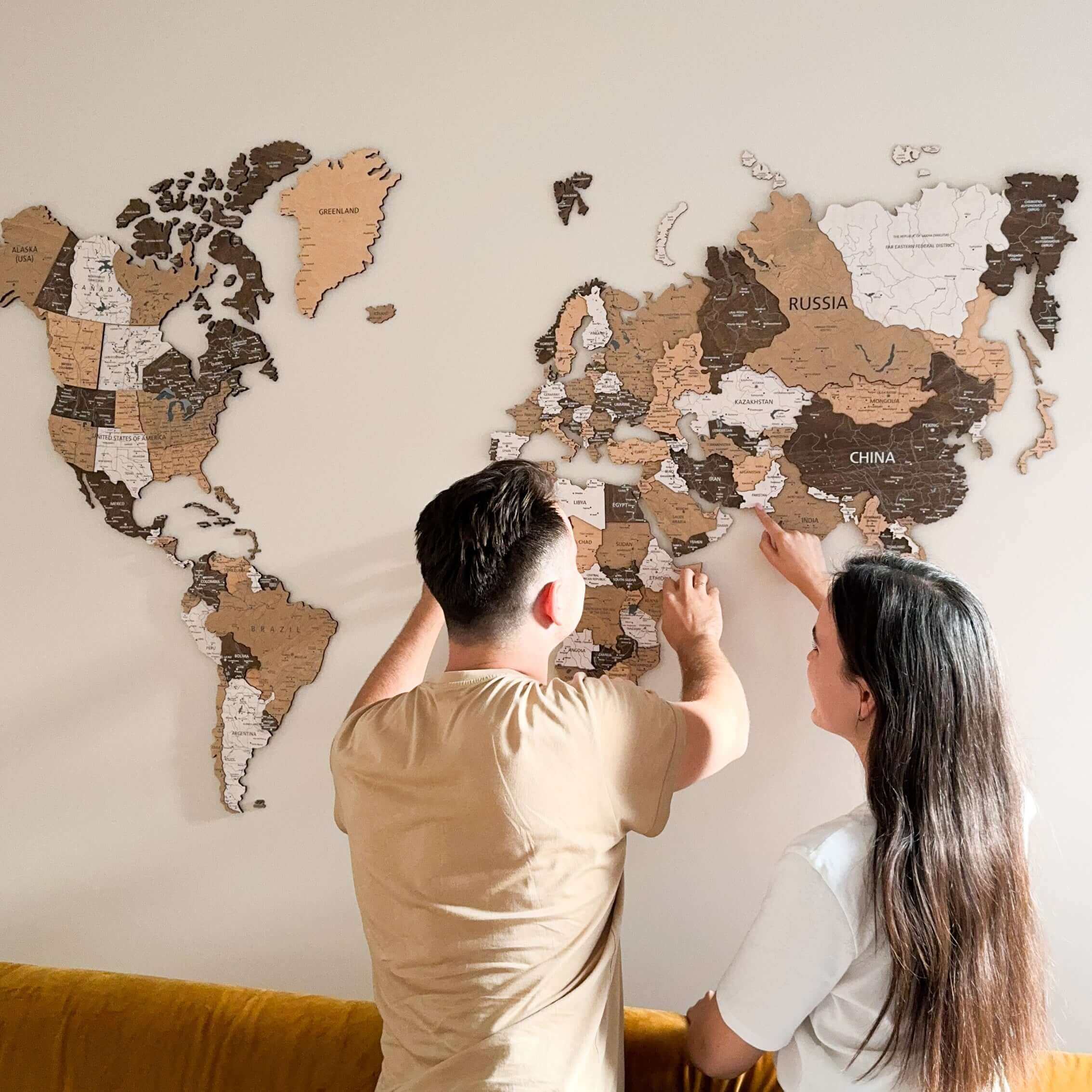 Couple assembling a 3D wood world map on wall, showcasing light brown layers and intricate details.