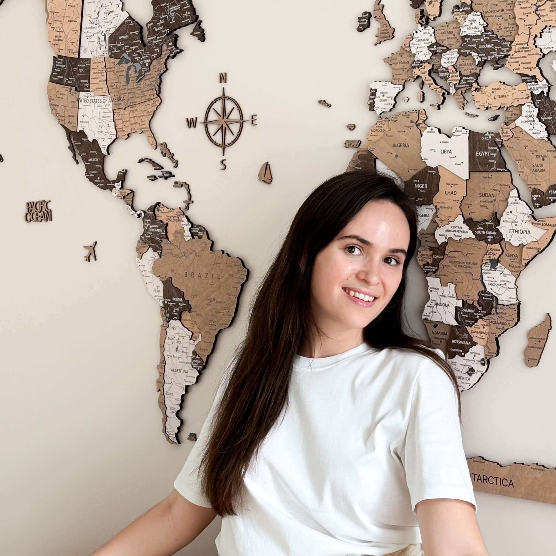 Woman posing next to a 3D wood world map in light brown and dark brown shades, enhancing interior decor.